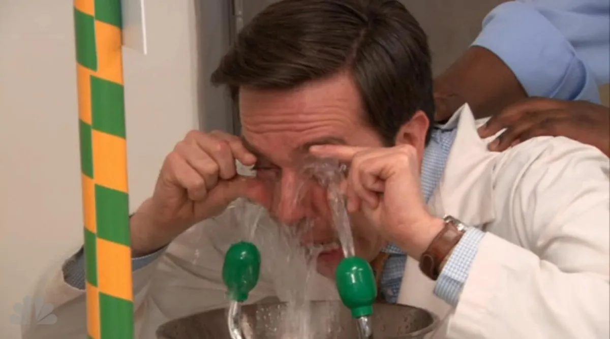 A man in a white lab coat is leaning over a sink with water forcefully streaming from both eyes into a metal basin below. He…
