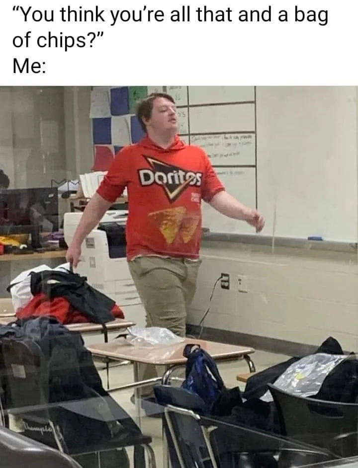 A person wearing a red Doritos-branded hoodie stands in a classroom with arms outstretched and head tilted back, appearing…