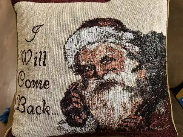 A close-up of a woven tapestry pillow featuring a stern-looking Santa Claus with a serious expression, next to the text 'I…