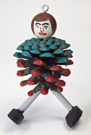 A handcrafted pinecone ornament with a painted cartoon face, red and teal painted scales, and two metal legs with black…