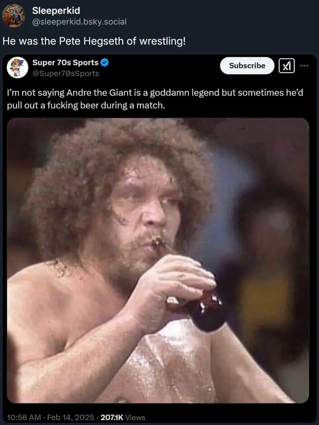 A shirtless man with a large afro and beard is drinking from a dark glass bottle during what appears to be a wrestling…