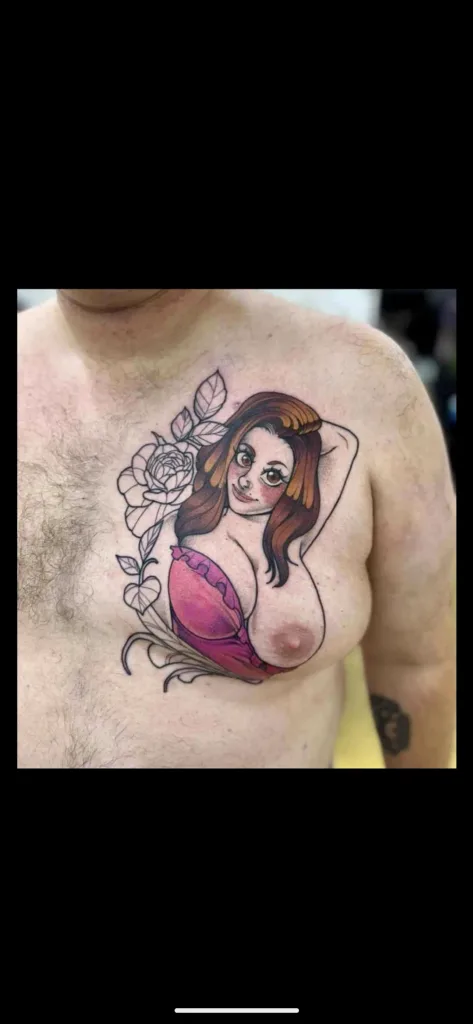 A man's chest displays a colorful tattoo of a stylized woman with long brown hair, wearing a pink bra, and a large rose…