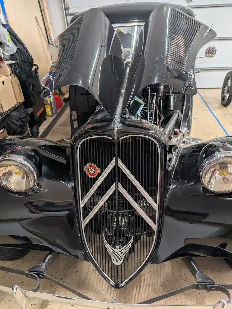 A close-up photo of a glossy black vintage car with its hood open, revealing the engine, parked in a garage. The car…