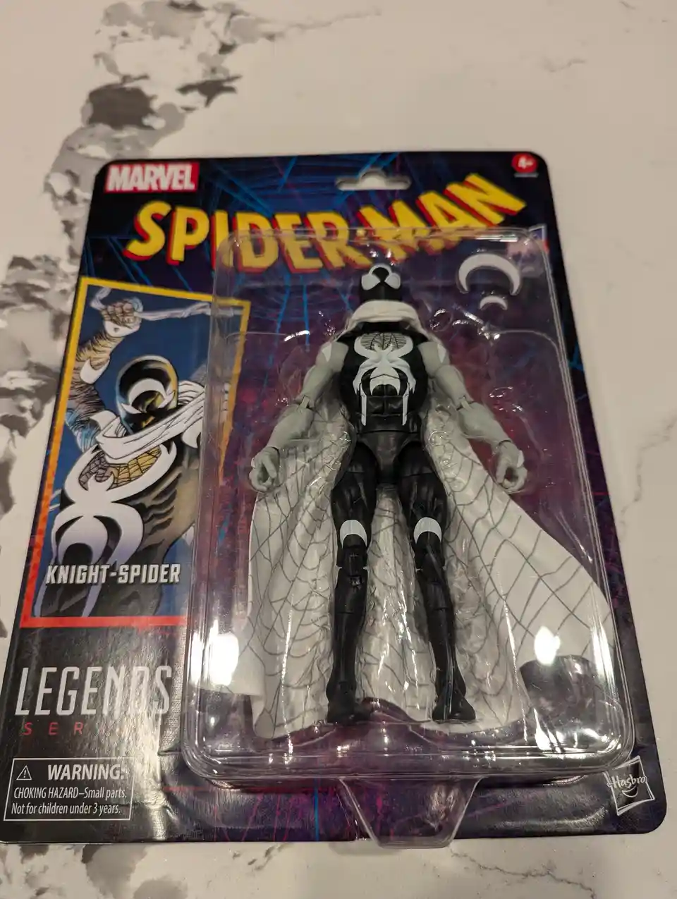 A Marvel Legends Series action figure of Knight-Spider, a black and white Spider-Man variant with a spider emblem on the…