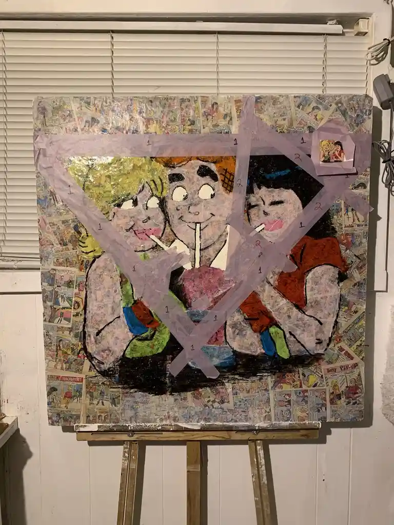 A handmade collage painting on an easel, featuring a cartoon-style depiction of Archie, Betty, and Veronica, is covered with…