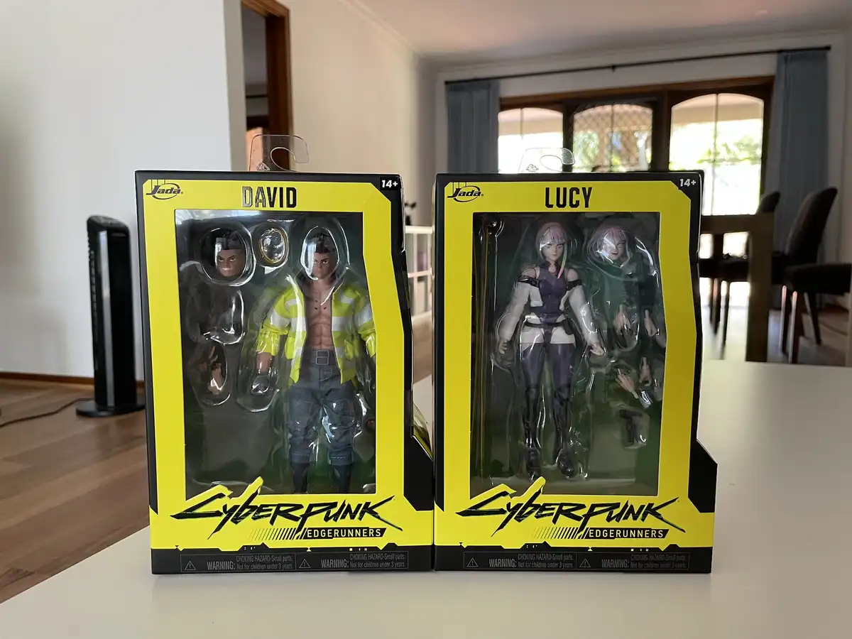 Two 'Cyberpunk Edgerunners' action figure boxes from Jada Toys sit side-by-side on a table, one labeled 'DAVID' and the…