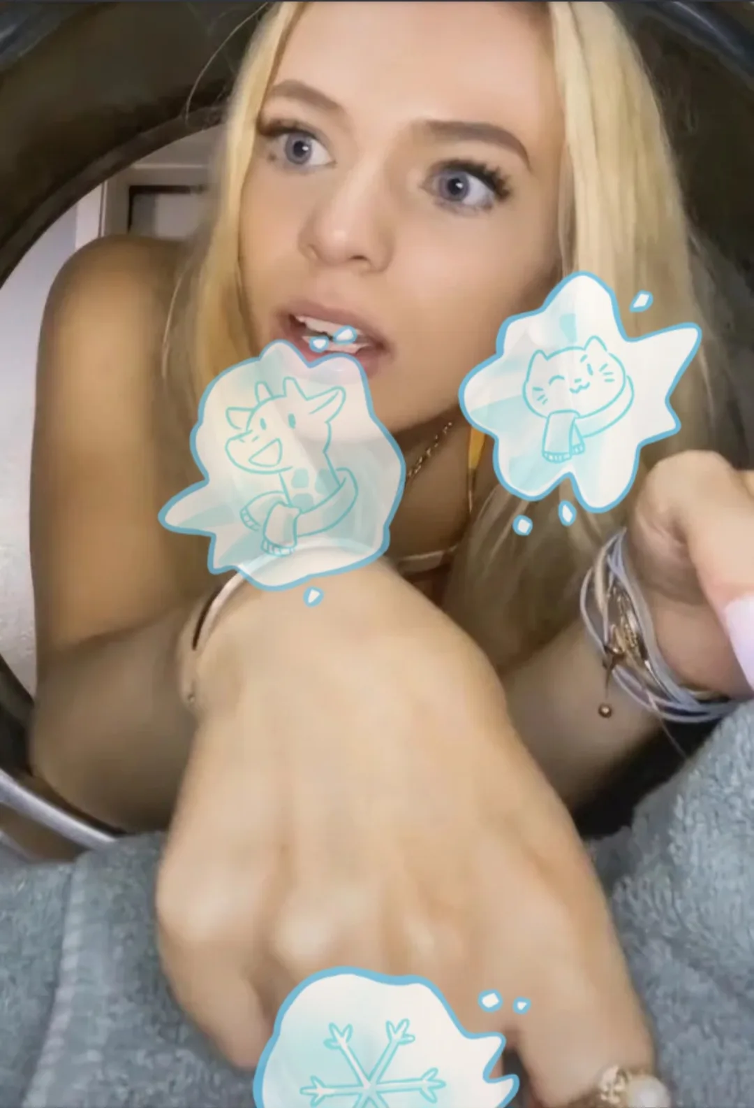 A blonde woman with wide eyes and an open mouth looks surprised or chilly, with three cartoonish ice-themed thought bubbles…