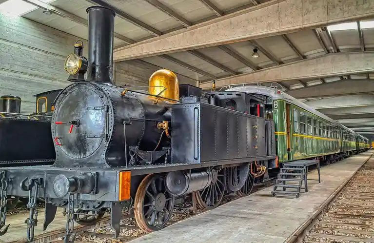 A black steam locomotive with a golden dome is parked indoors next to green passenger cars. The overlaid text reads 'i'm not…
