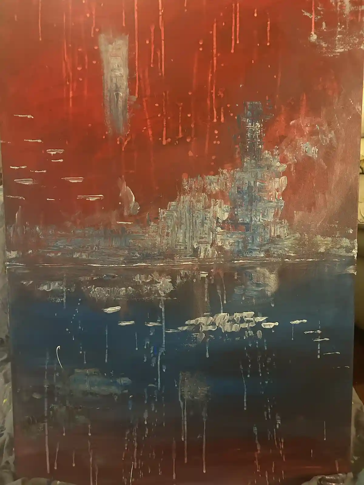 A painting depicts a cityscape with buildings rendered in gray and white against a red sky, with paint drips and splatters…